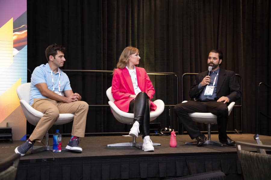 Three panelists speak to one another in front of a crowd.