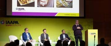 Panelists on stage with a PowerPoint slideshow on a projector screen showing food and beverage offerings as example during F&B Innovations panel at IAAPA Expo Europe