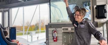 A ride operator clears a train by raising her left arm over her head and smiles at guests