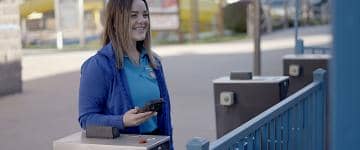 An amusement park employee smiling and holding a smartphone with a mobile scanner to scan ticket entry