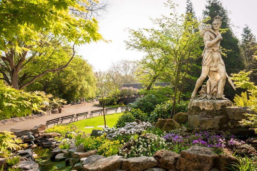 A garden area with a statue overlooking the flowers and walking path inside Antwerp Zoo in Belgium