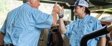 Two Silver Dollar City amusement park employees wearing their designated uniforms, fist-bumping with thumbs up 